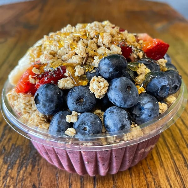 Krave Juice Bar's acai bowl with blueberries, strawberries, granola, and honey on a wooden table.