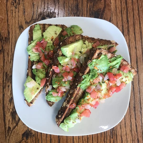 Three slices of avocado toast with diced tomatoes and onions on a white plate.