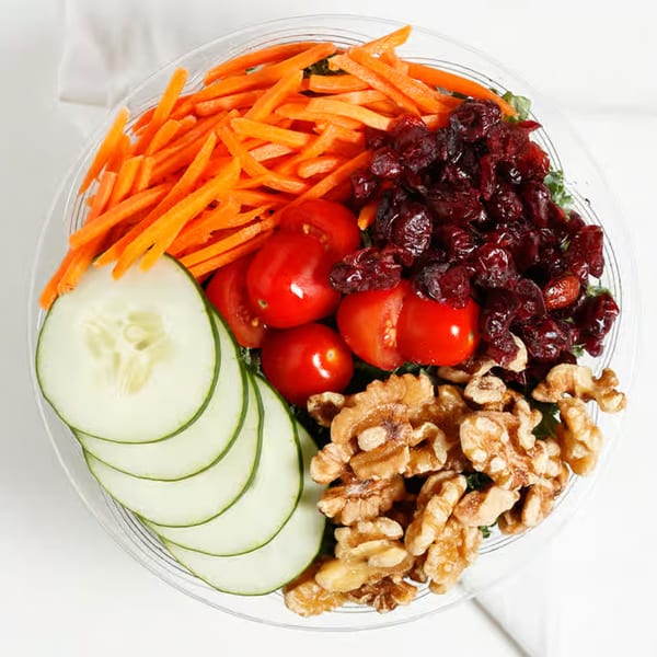 Overhead view of a Krave Juice Bar salad with carrots, cranberries, tomatoes, cucumbers, and walnuts.