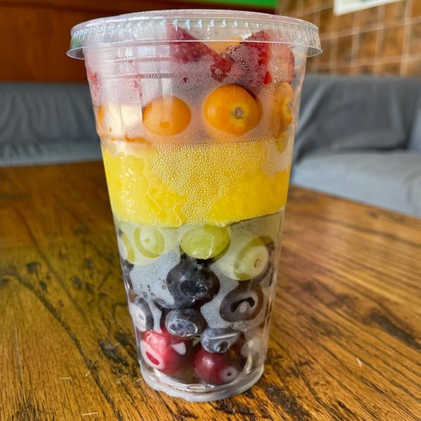 A clear plastic cup filled with colorful layers of fresh fruit, including berries, grapes, and citrus.