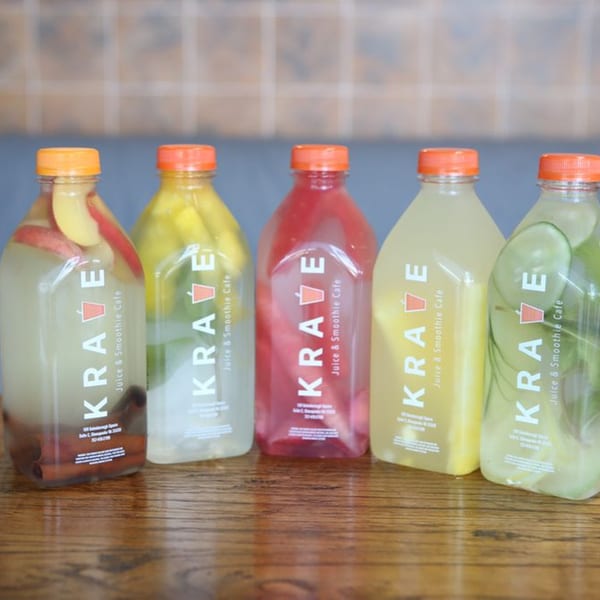 Five Krave Juice Bar bottles filled with colorful fruit-infused drinks on a wooden table.