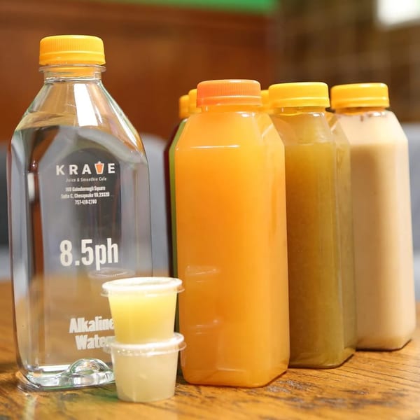 Krave Juice Bar's alkaline water bottle, various juice bottles, and two small shot cups on a wooden table.